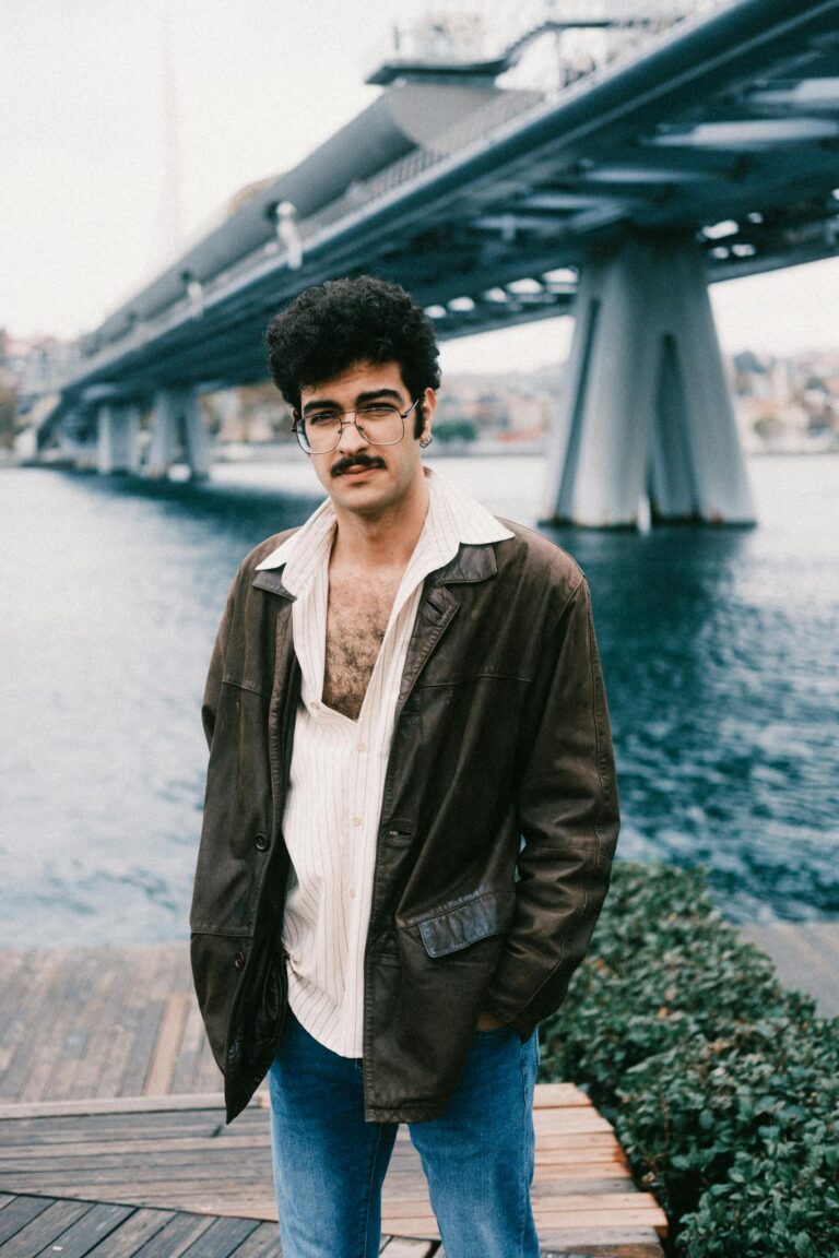 Man in casual attire standing by water with a bridge backdrop in Istanbul.